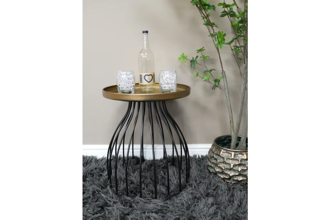 Round gold and black metal side table with decorative glasses and bottle on grey rug