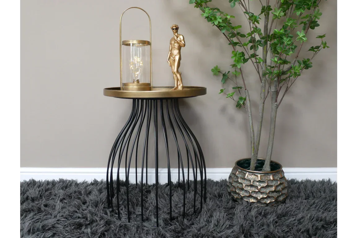 Round side table with gold top, black metal legs, decorative lamp and statue beside plant