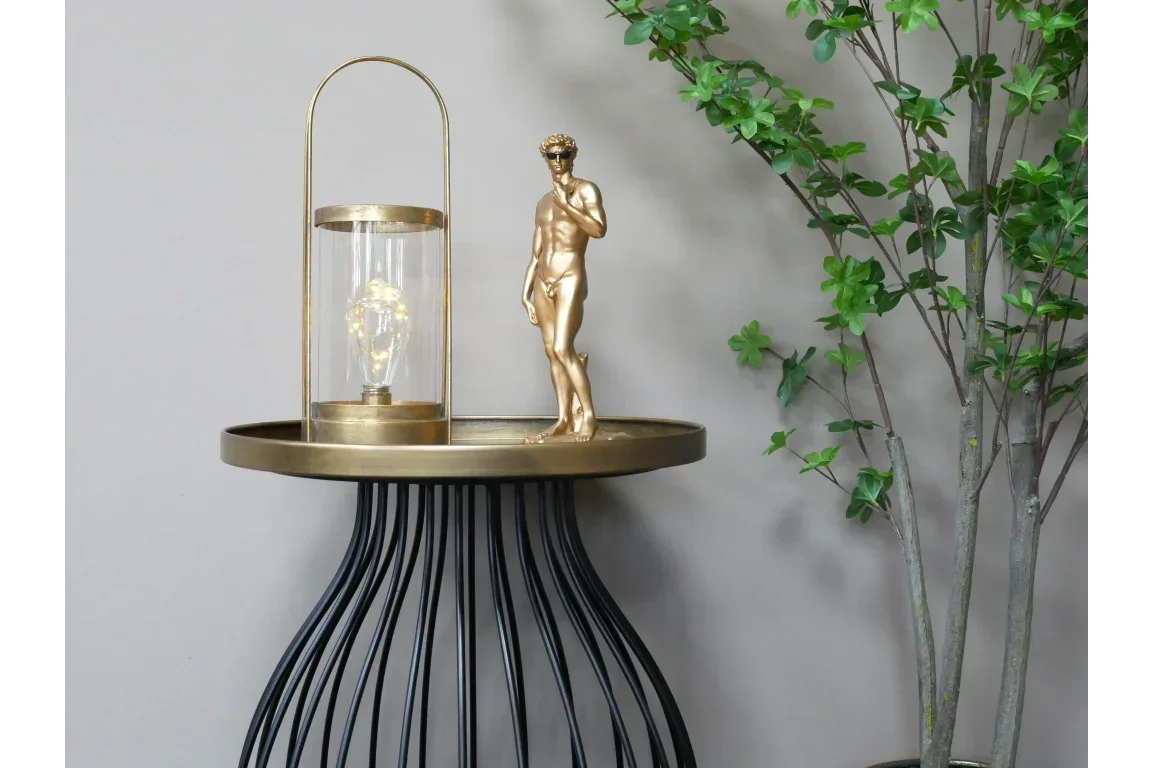 Gold accent table with black wire base, glass lantern, gold statue, and faux leafy plant