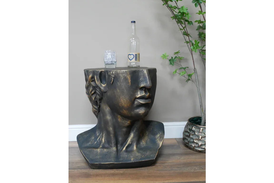 bronze effect head sculpture side table with glass and bottle on top beside potted plant