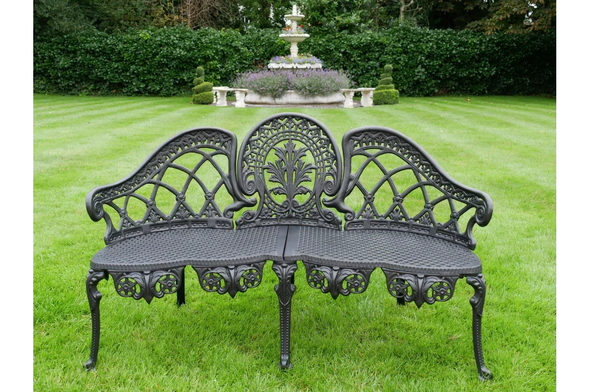 Black cast iron garden bench with ornate backrest on green lawn with fountain