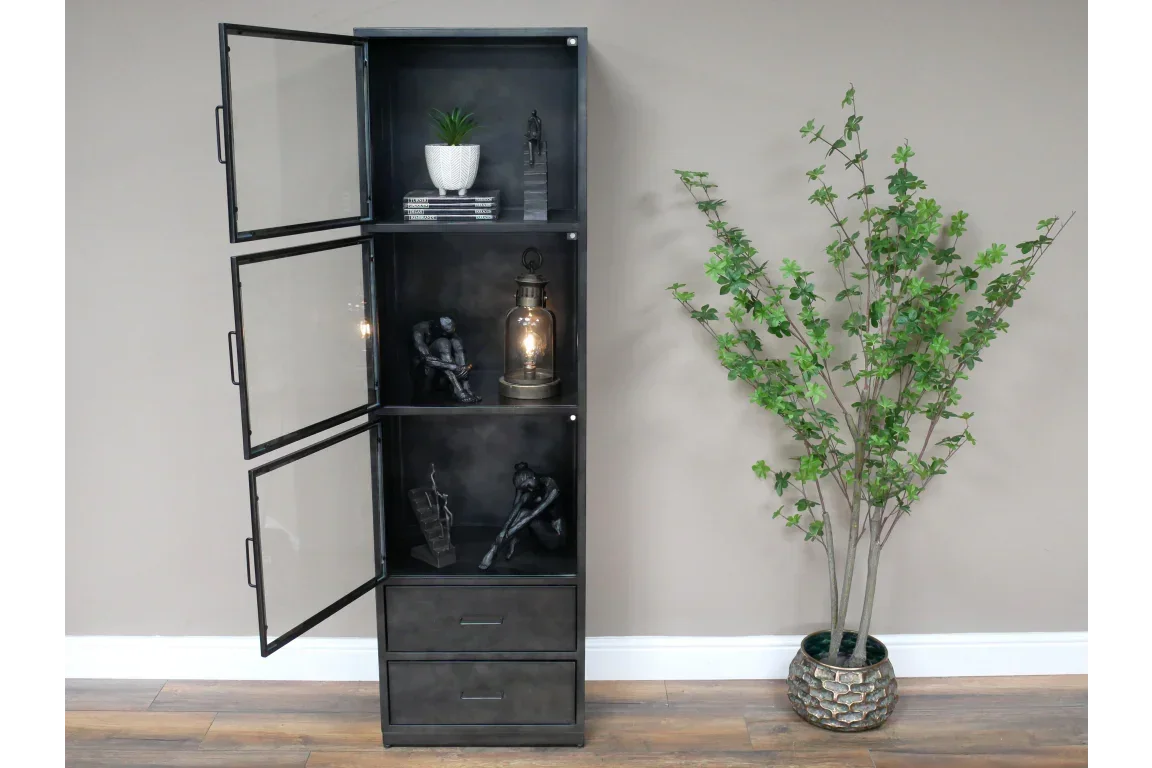 Tall black metal display cabinet with glass doors and drawers beside potted artificial plant