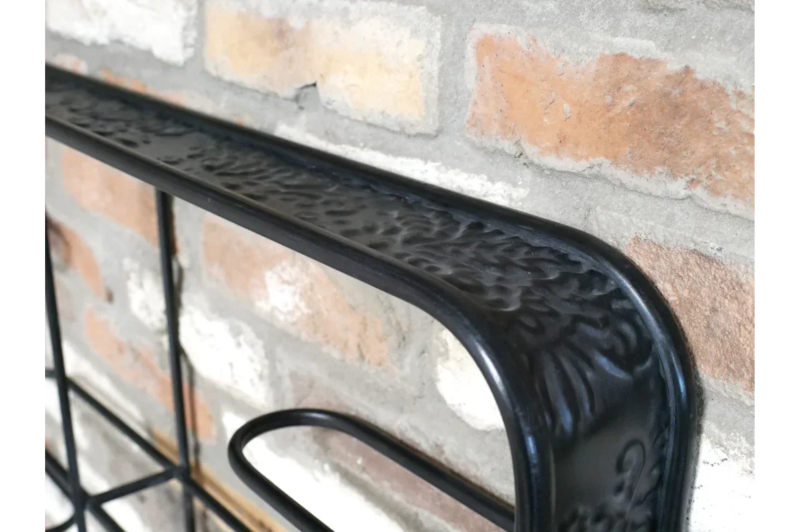 Close up of black metal shelf with embossed detail mounted on exposed brick wall