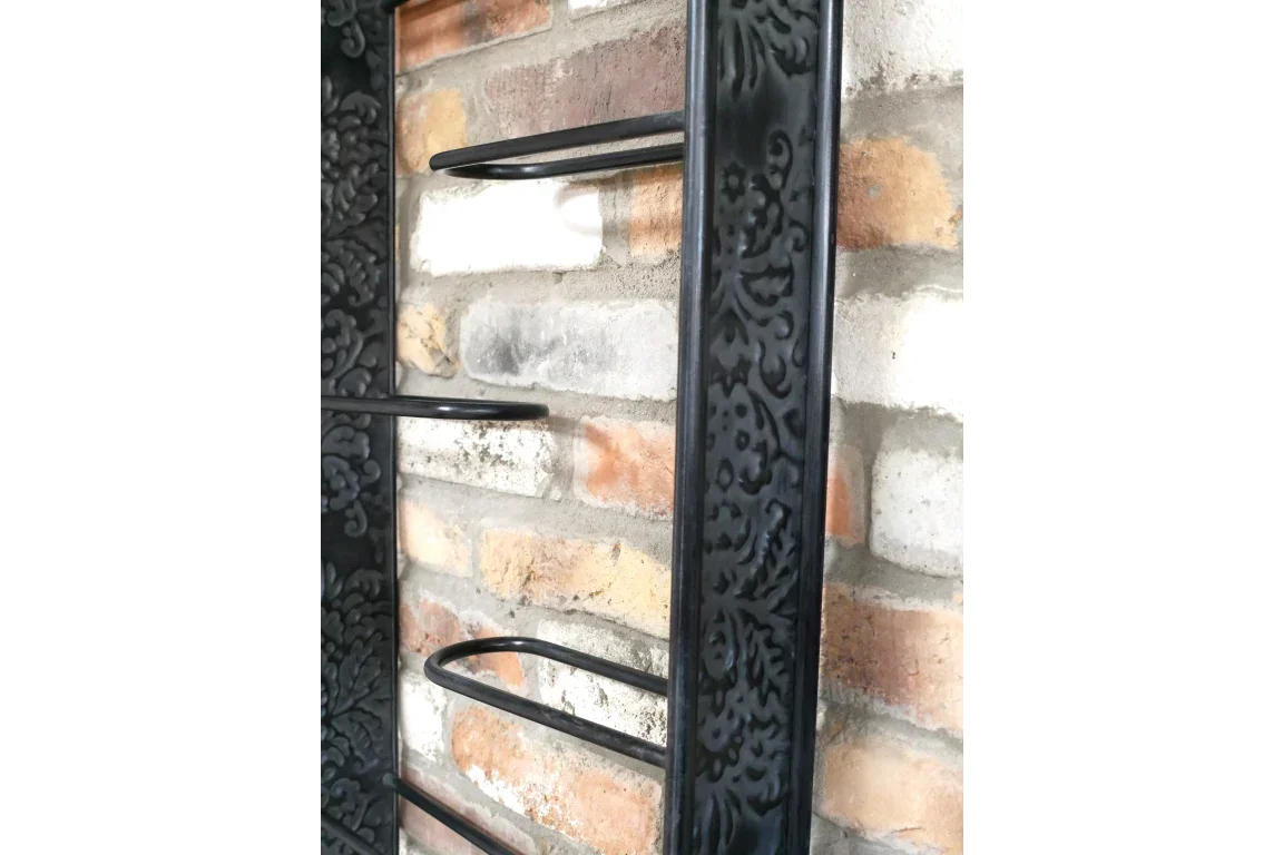 Black metal wall shelf with ornate floral pattern frame against brick wall