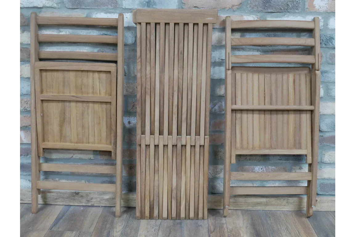 Folded wooden garden chairs and table set against brick wall