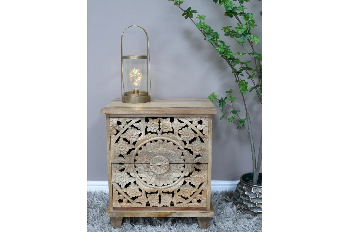 Carved wooden bedside table with floral pattern, brass lantern, and artificial plant