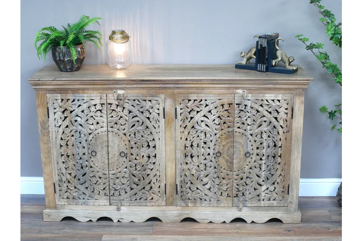 Carved wooden sideboard cabinet with ornate doors, decorative plant, lamp, and bookends