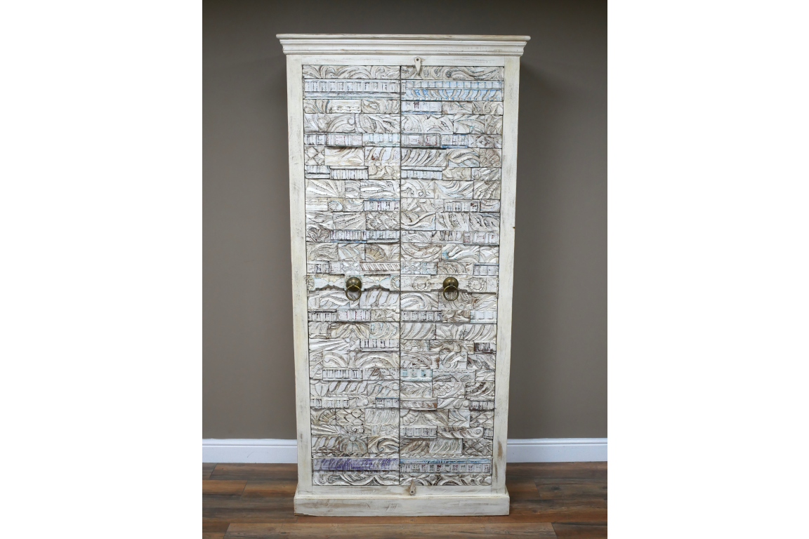 Large wooden cabinet with intricate carved patterns, whitewashed finish, two metal ring handles, standing on wooden floor.