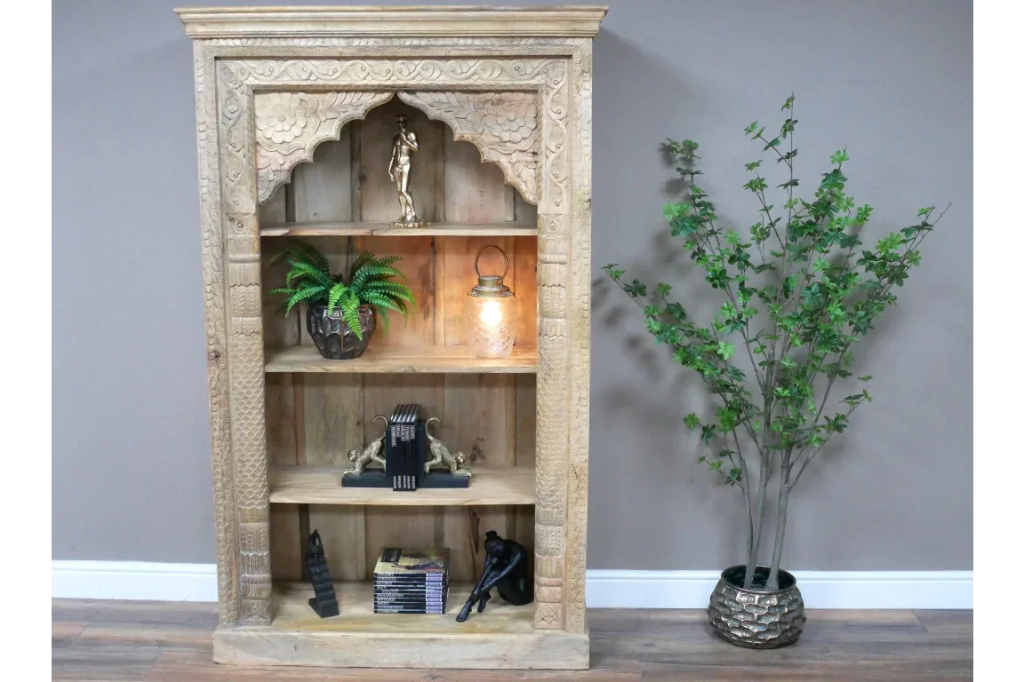 Carved wooden bookcase with open shelves and decorative items, beside artificial plant