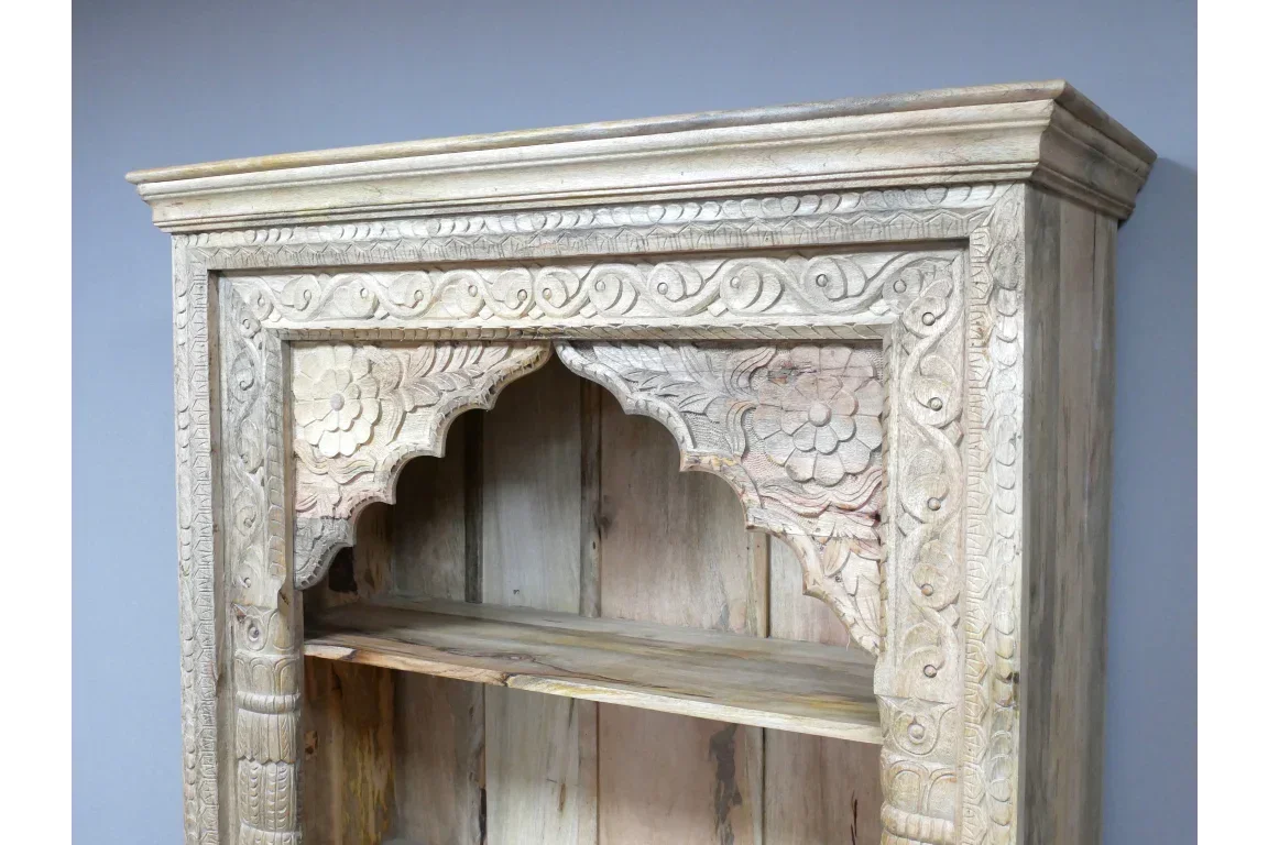 Carved wooden bookcase with ornate floral detailing on top shelf and light natural finish
