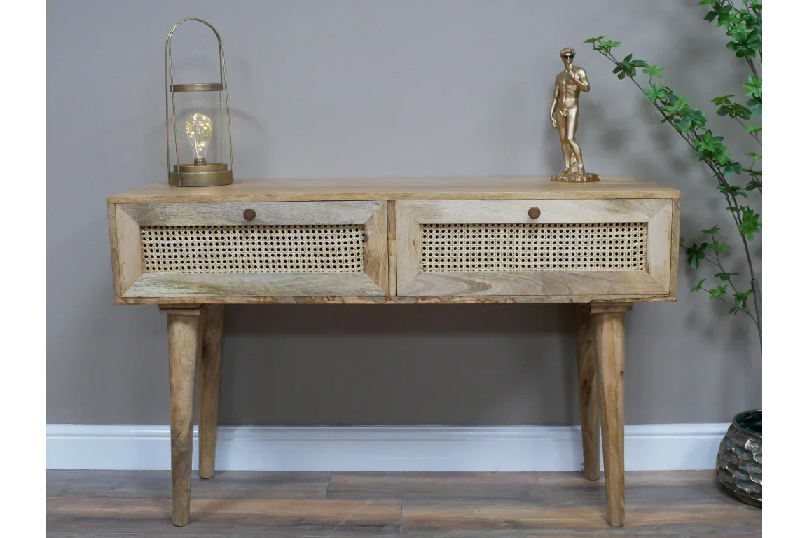 Wooden console table with cane drawers, two decor pieces, and plant against grey wall