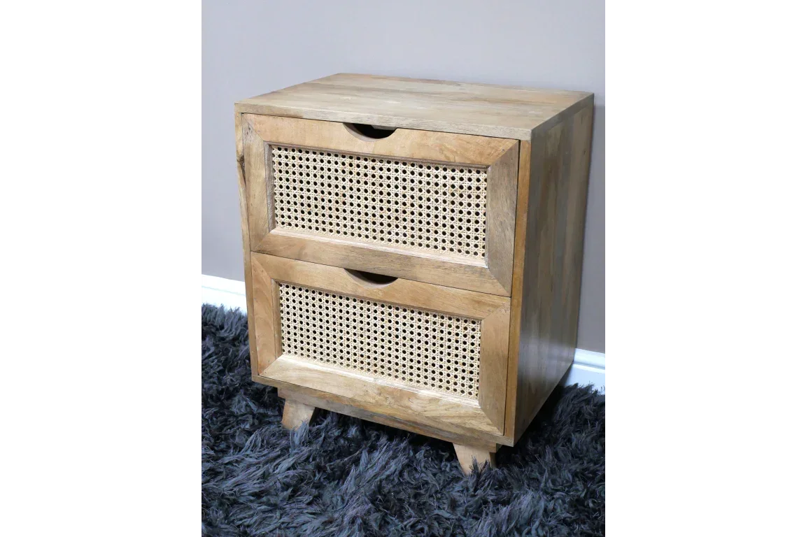 Wooden bedside table with two rattan drawers on a dark rug against grey wall