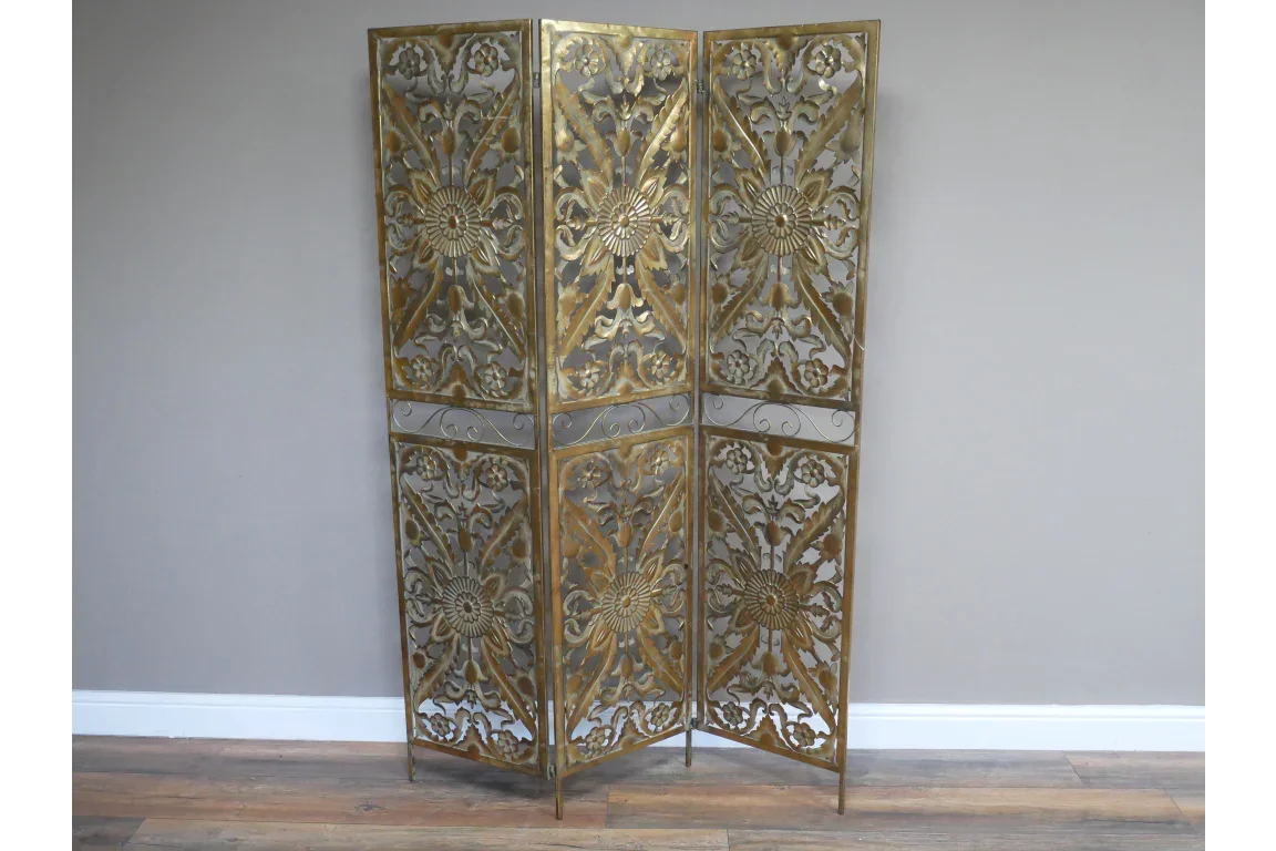 Gold metal room divider with floral cut-out panels standing on wooden floor
