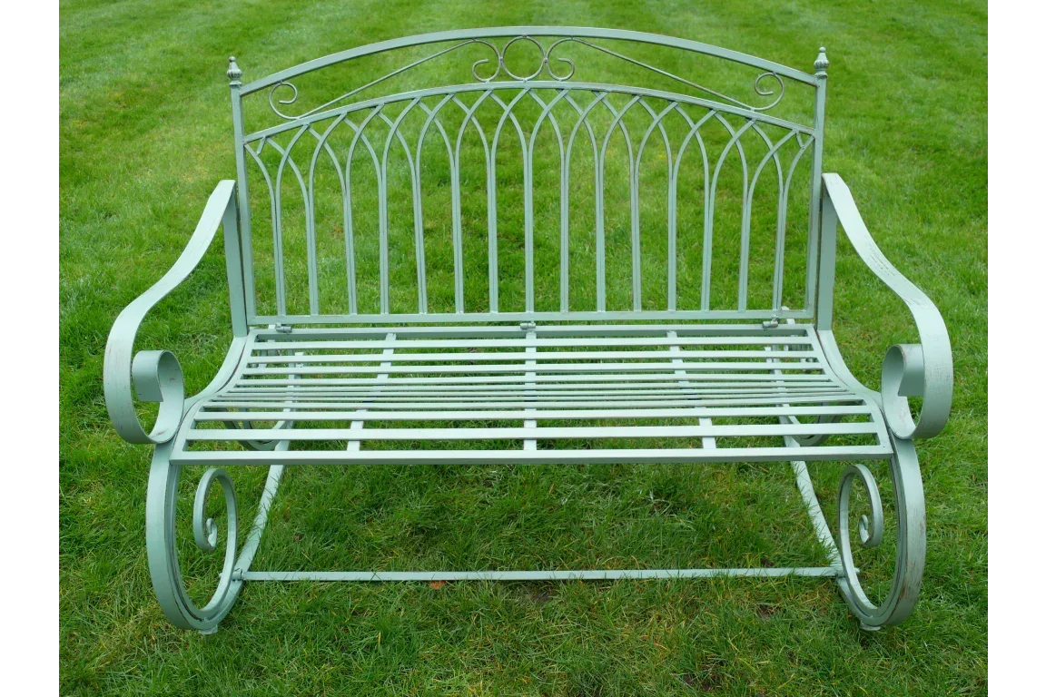 Metal garden bench with ornate backrest and curved armrests on green lawn