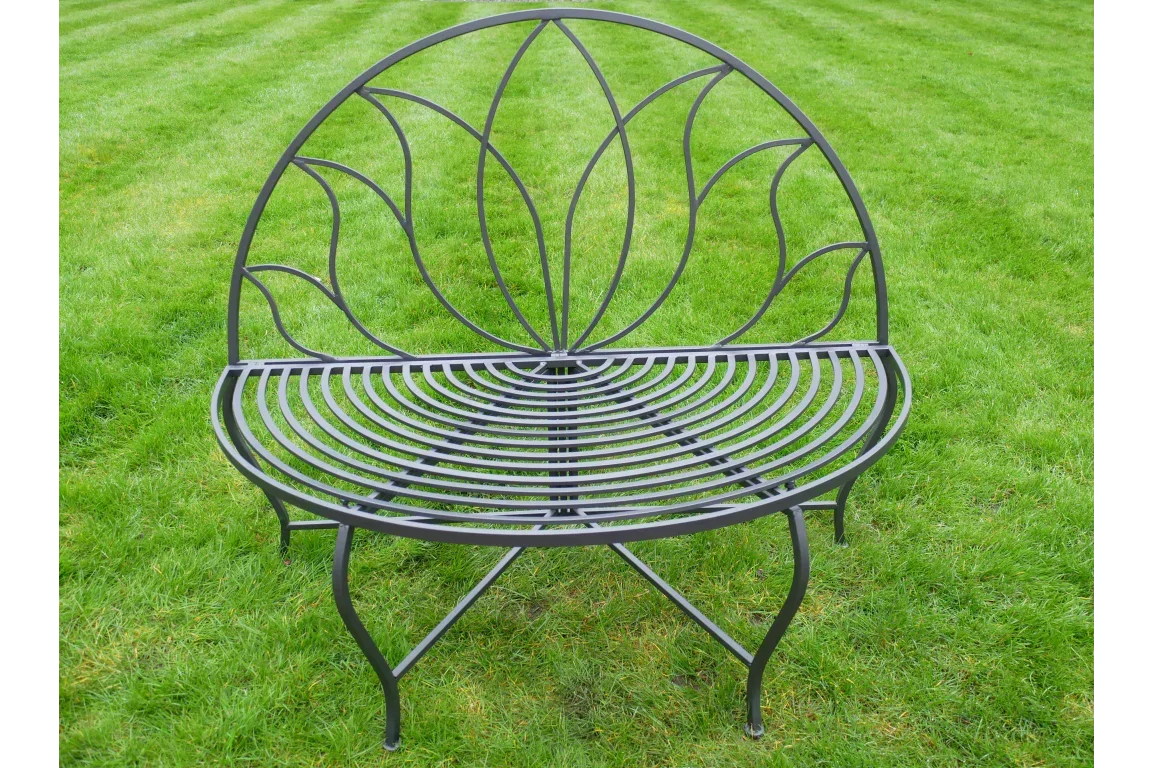 Black metal garden bench with curved seat and decorative backrest on grass lawn