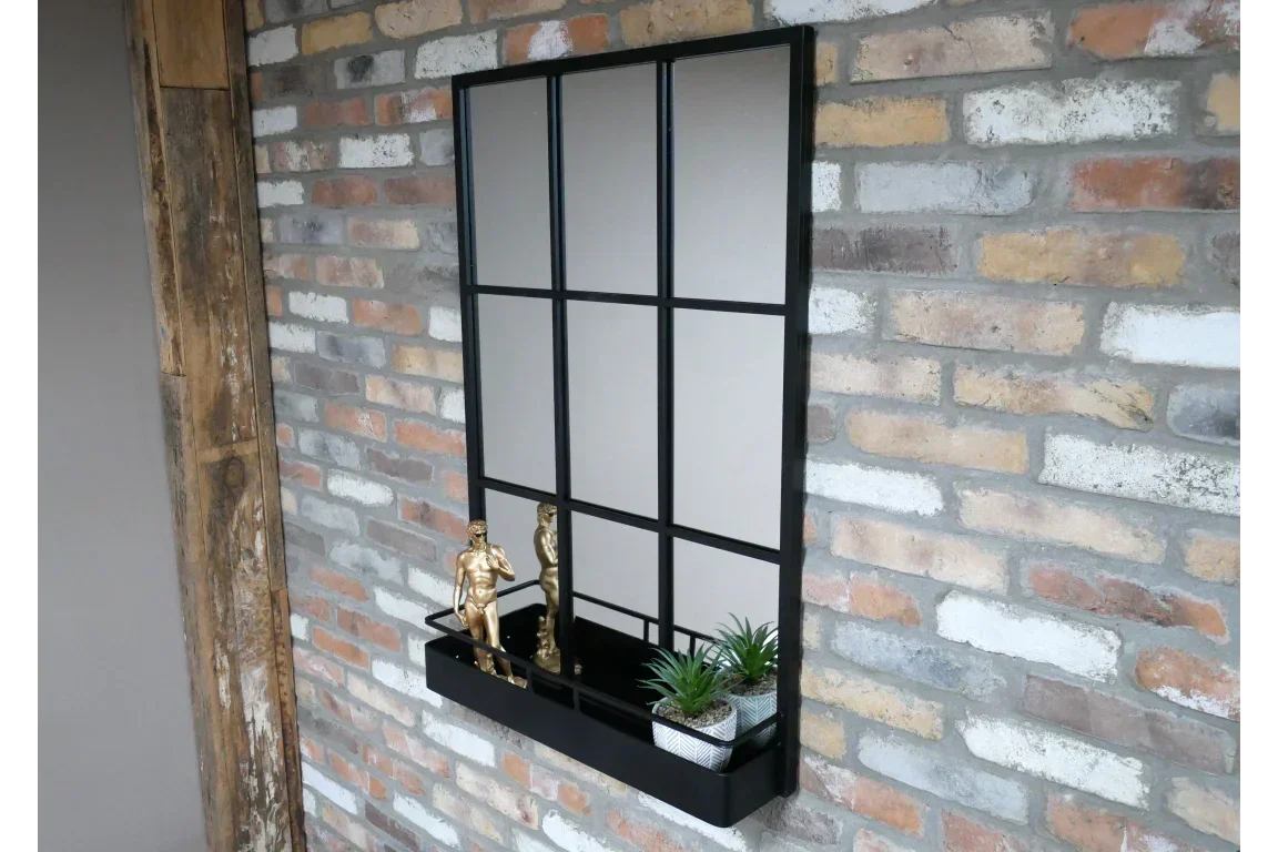 Black metal wall mirror with shelf, gold figurines, and small potted plants on brick wall