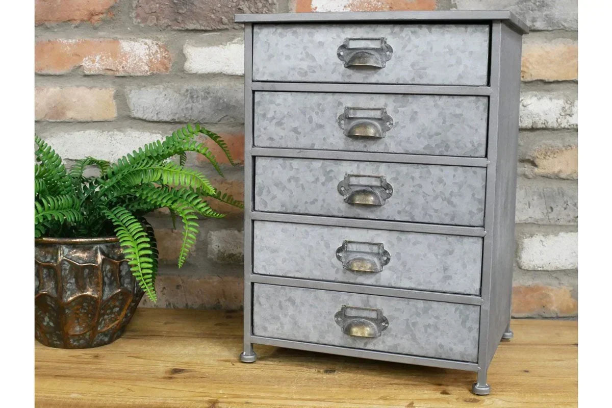 Galvanised metal storage drawers with cup handles on wooden surface beside potted fern