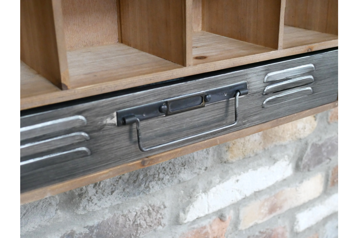 Close-up of wooden wall unit with metal drawer handle and cubby compartments against a stone wall background.
