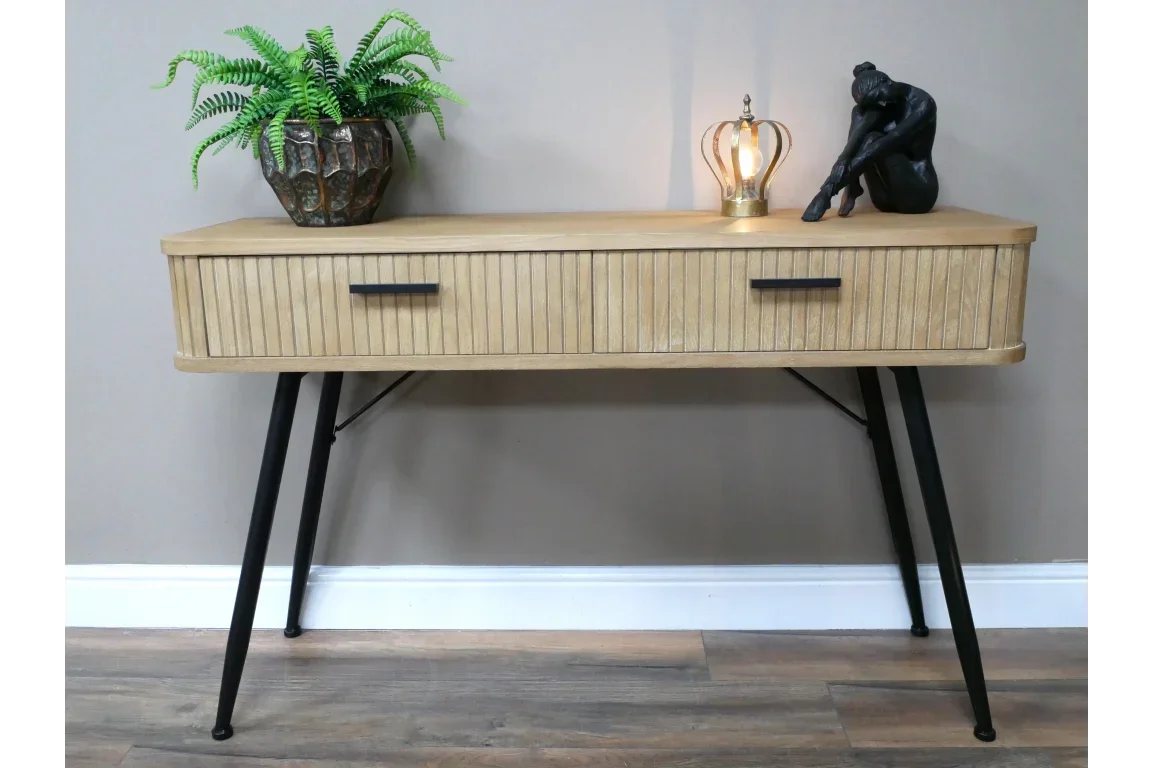 Wood console table with black legs, two drawers, plant, lamp, and sculpture decor