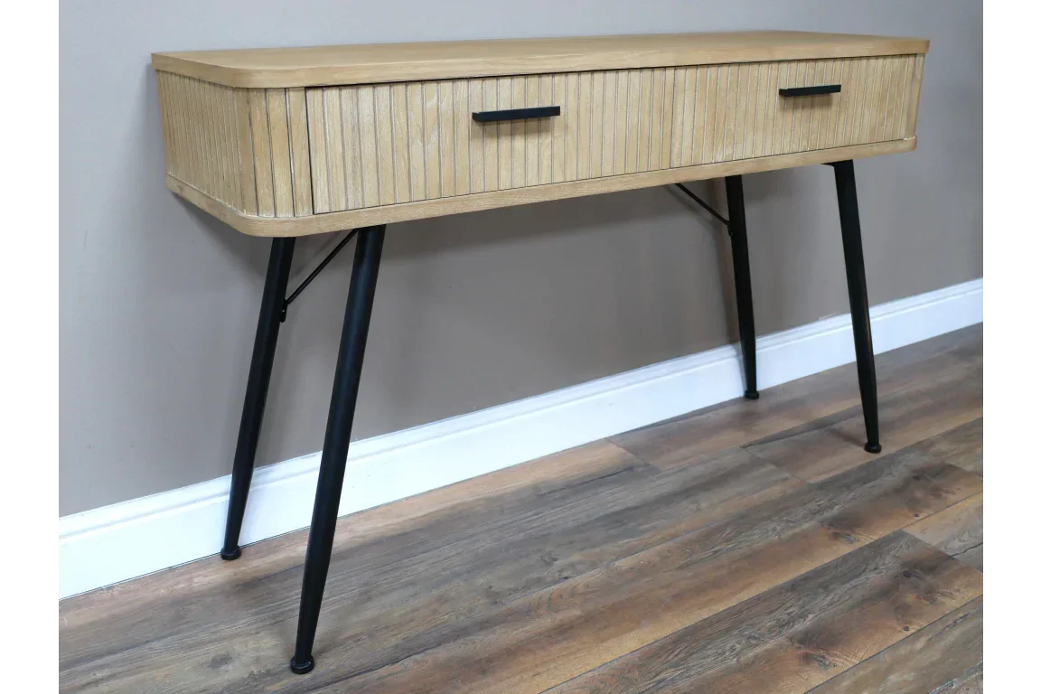 Wood console table with ribbed front, black metal legs and dual drawers against wall