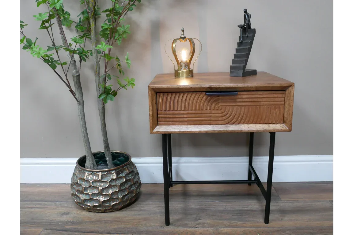 Wooden bedside table with black metal legs, geometric drawer front, lamp and statue on top