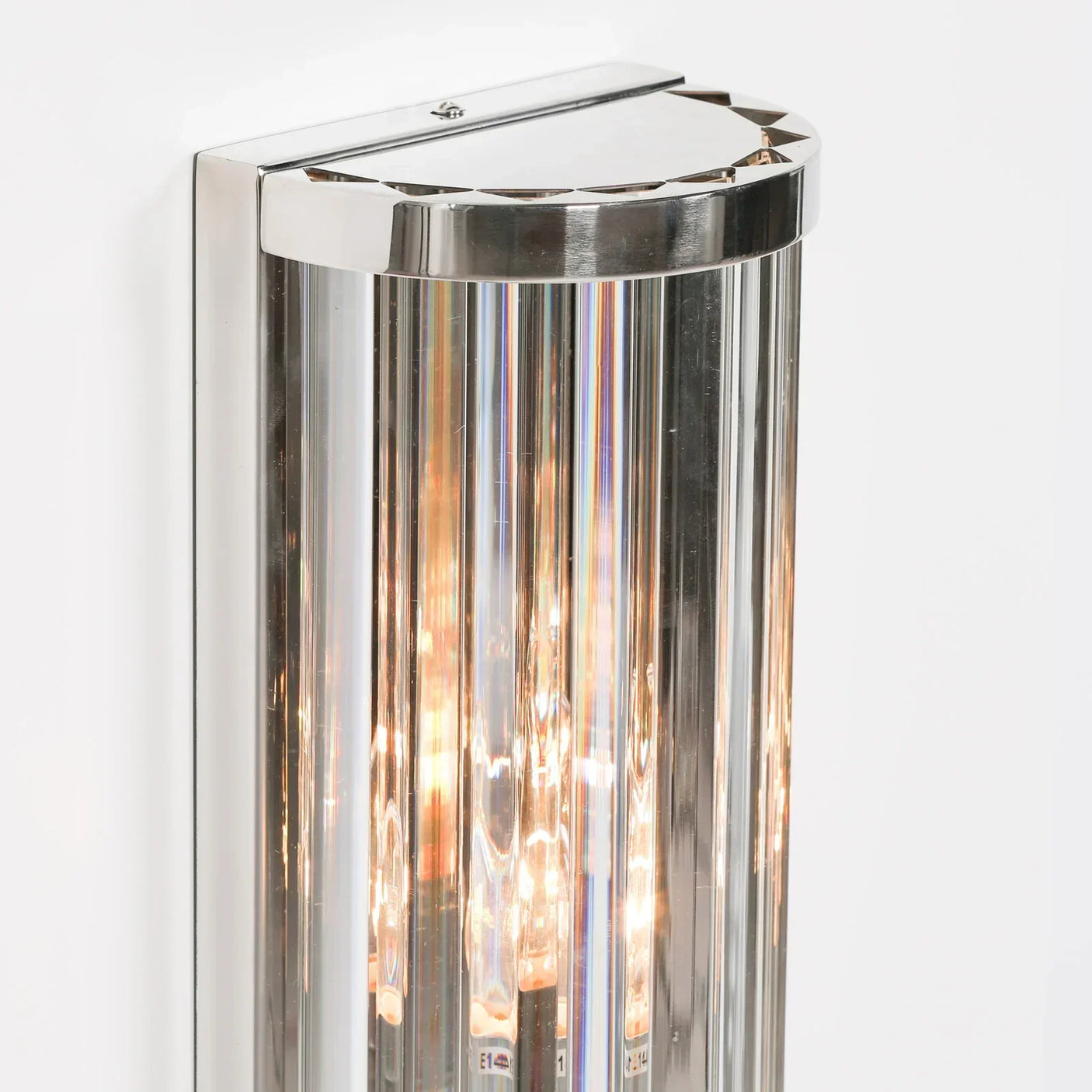 Modern wall light with chrome frame and vertical glass panels glowing on white wall