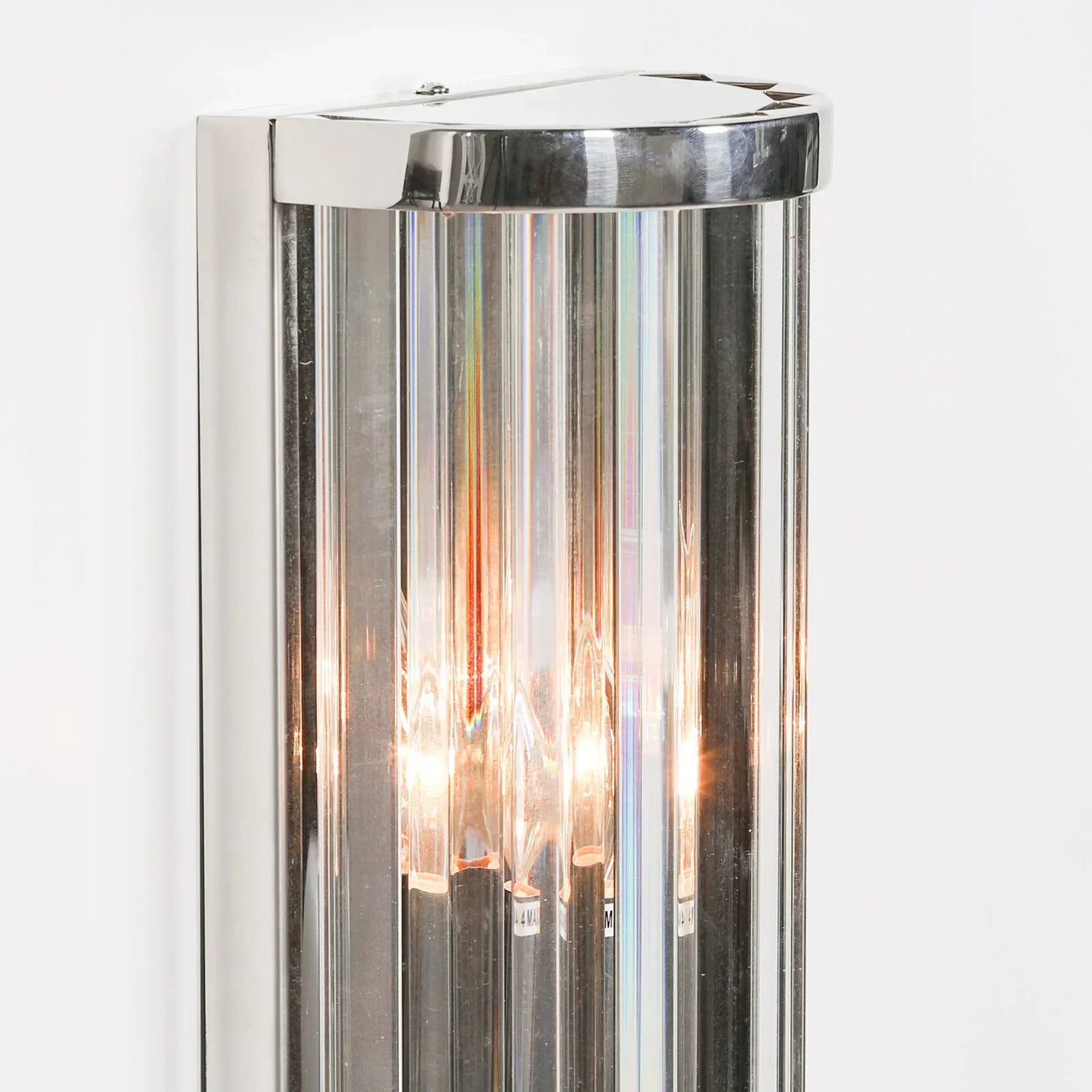 Chrome and glass wall light with vertical ribbed panels illuminated on white wall