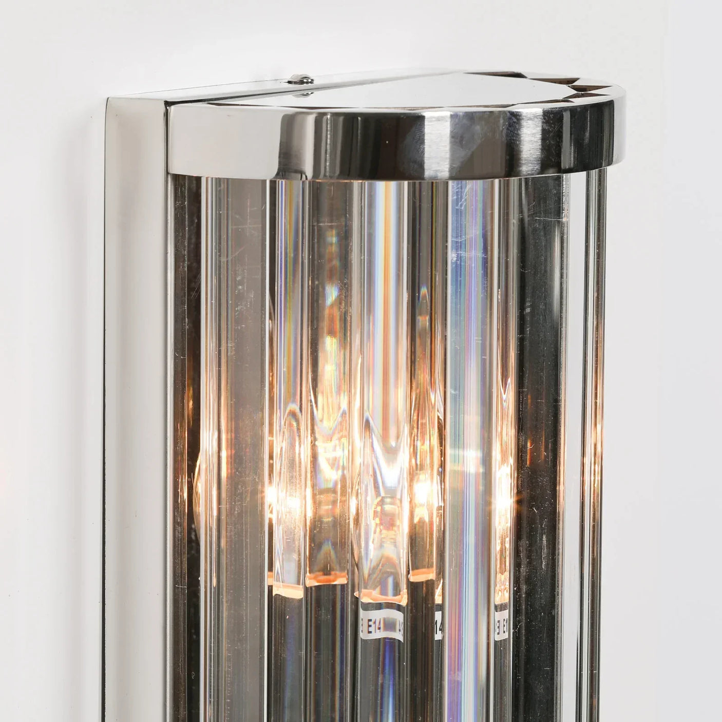 Chrome wall light with clear glass rods and visible bulbs mounted on white wall