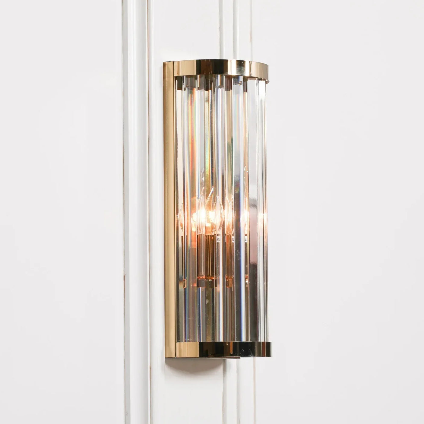 Gold and glass wall light fixture with vertical crystal panels mounted on white wall