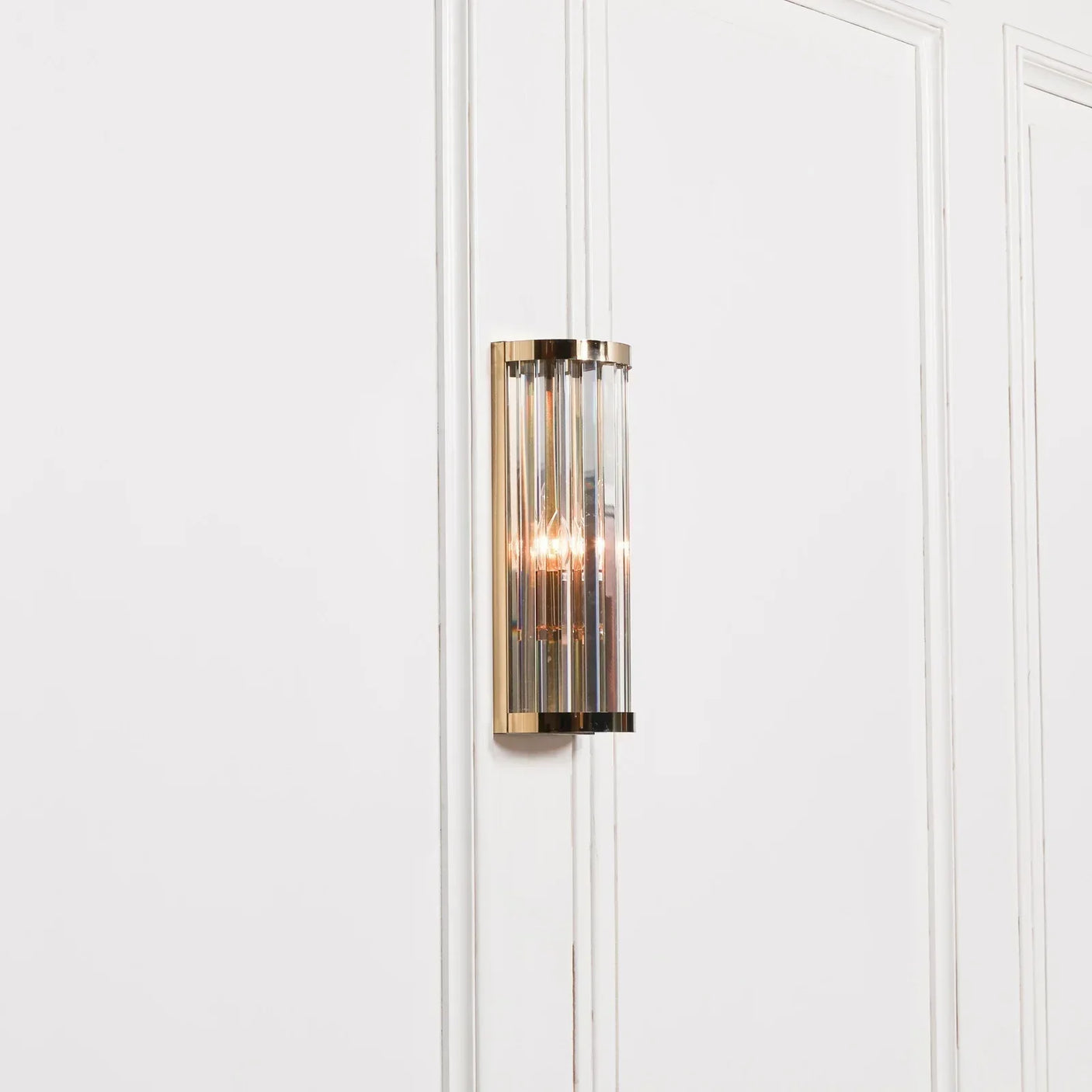 Gold and glass wall light fitting with vertical panels on white paneled wall