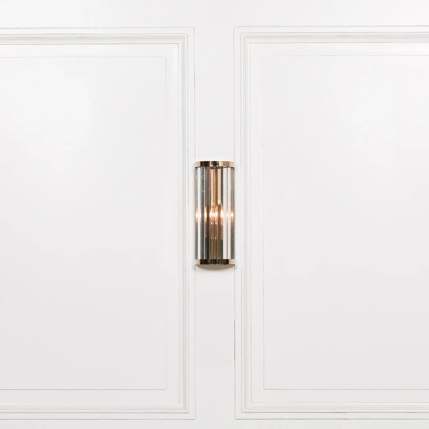Chrome and glass wall light fixture mounted on white panel wall