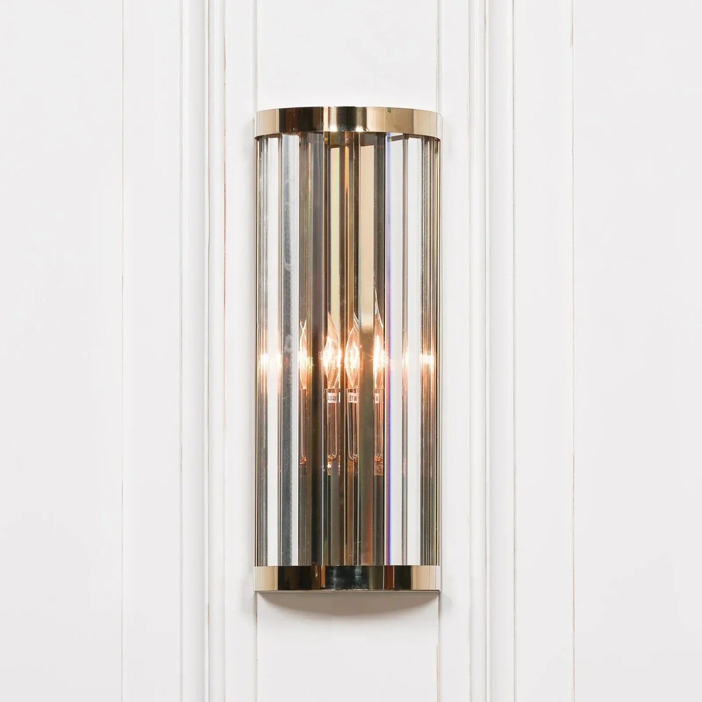 Brass and glass wall light fixture with vertical panels on white paneled wall