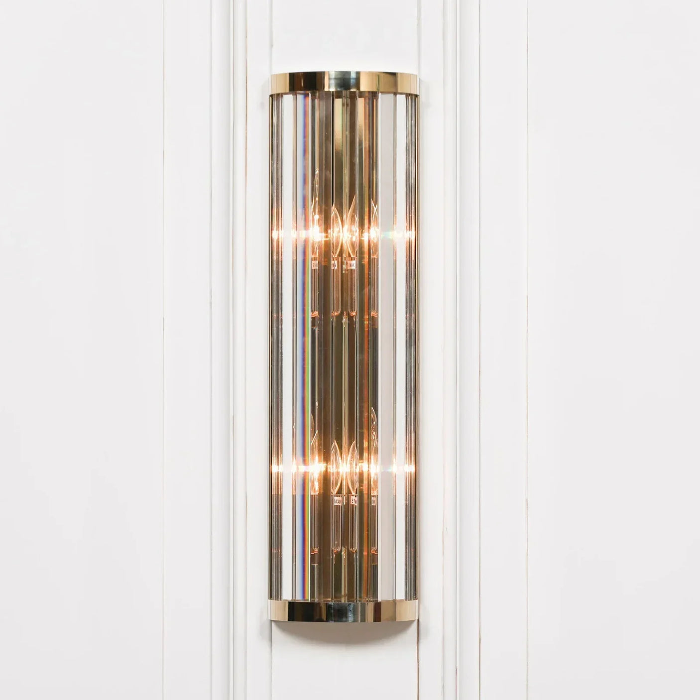 Brass and glass wall light fixture illuminated on white panelled wall