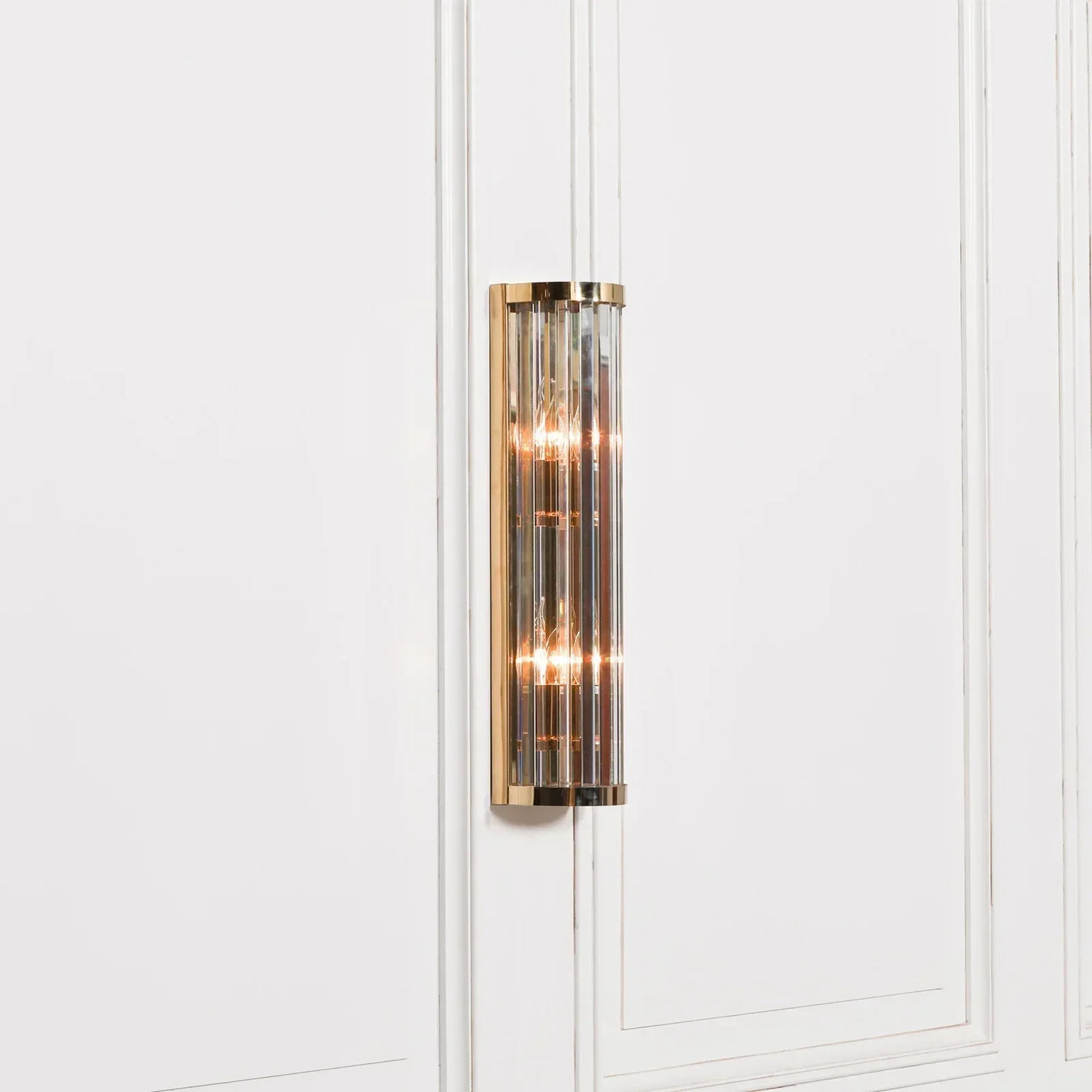Gold and glass wall light fixture mounted on white paneled wall