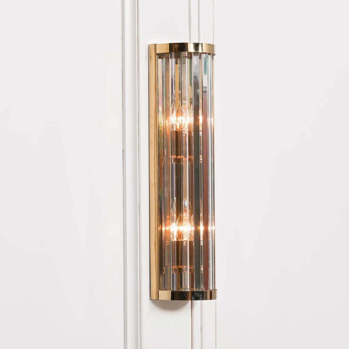 Gold and glass wall light fixture with vertical rods on white panelled wall
