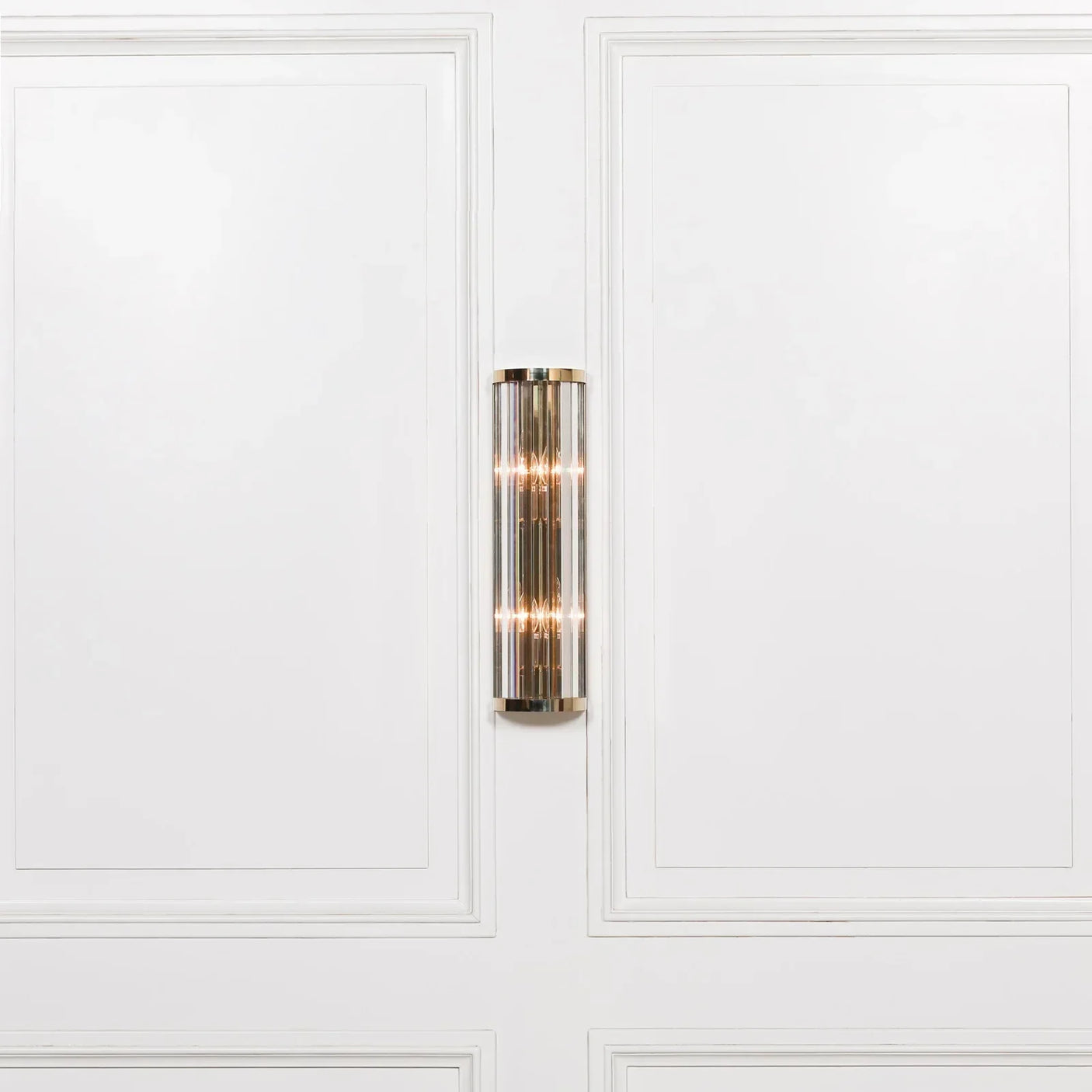 Gold wall light with glass rods mounted on white panelled wall