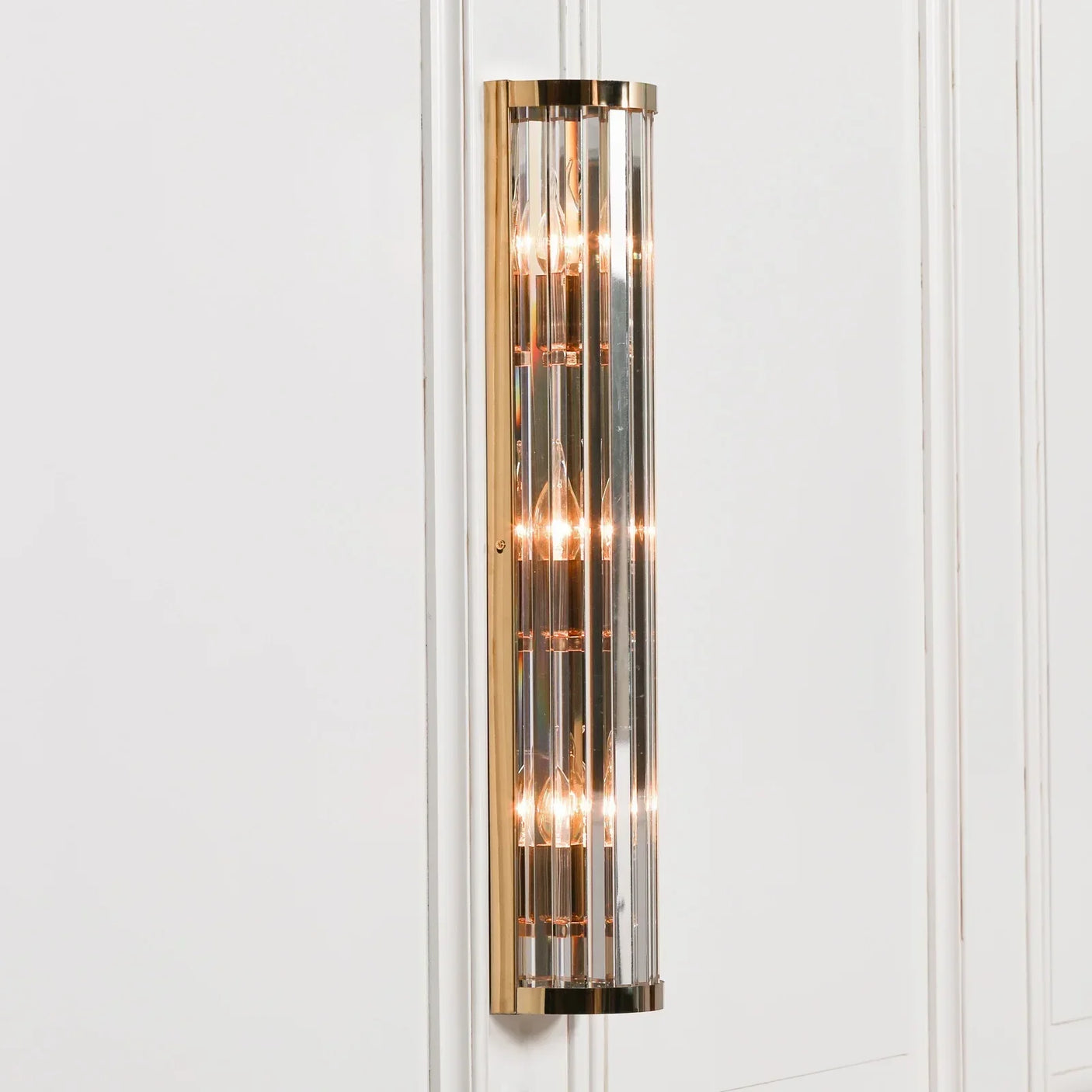 Gold and glass wall light fitting with vertical rods mounted on white panelled wall