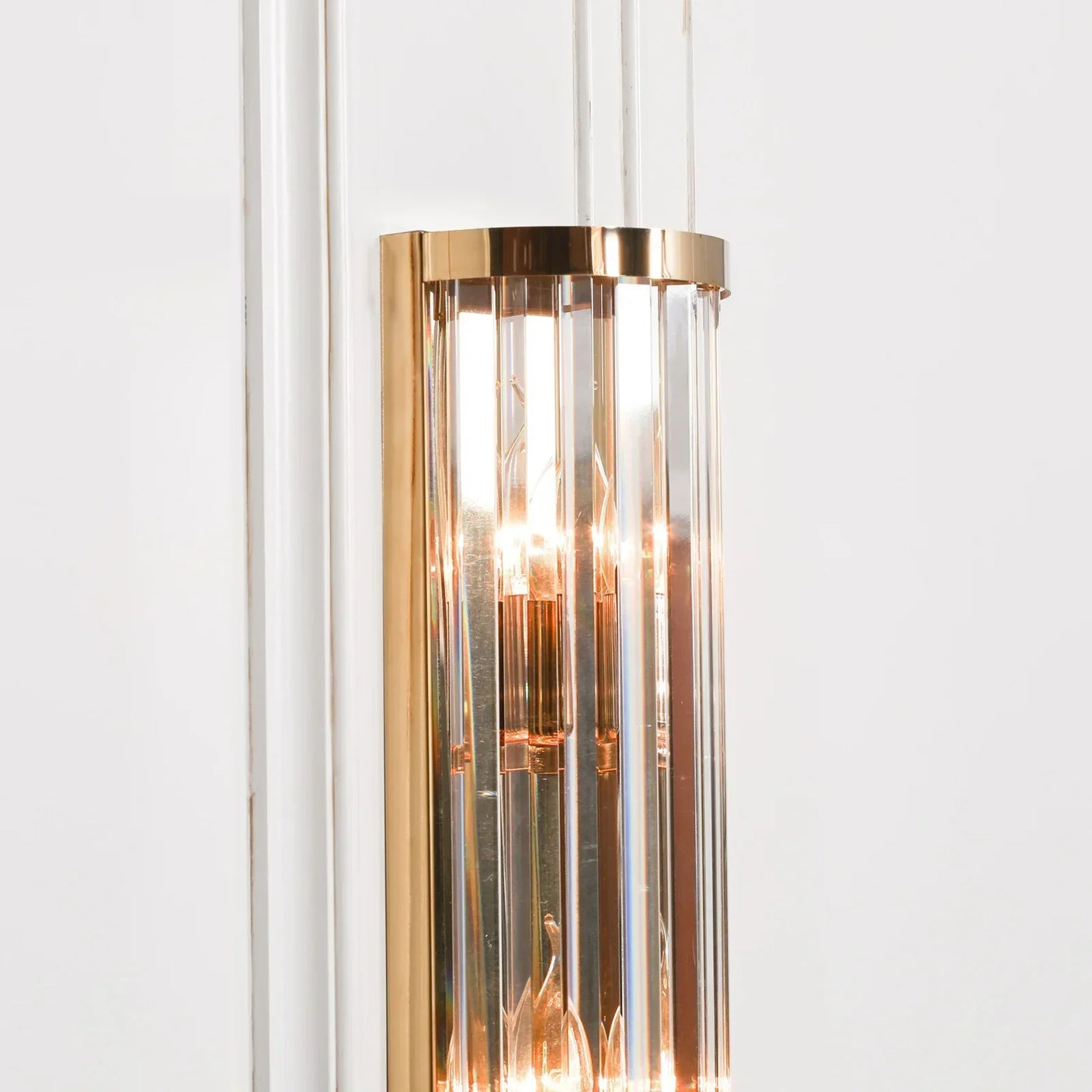 Gold and glass wall light fixture with vertical glass panels on white wall