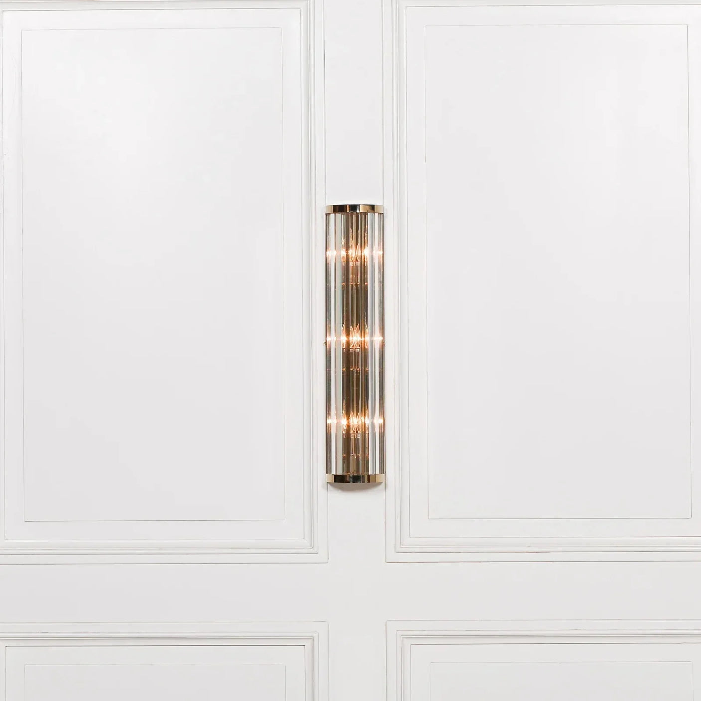 Chrome and glass wall light fixture mounted on white paneled wall
