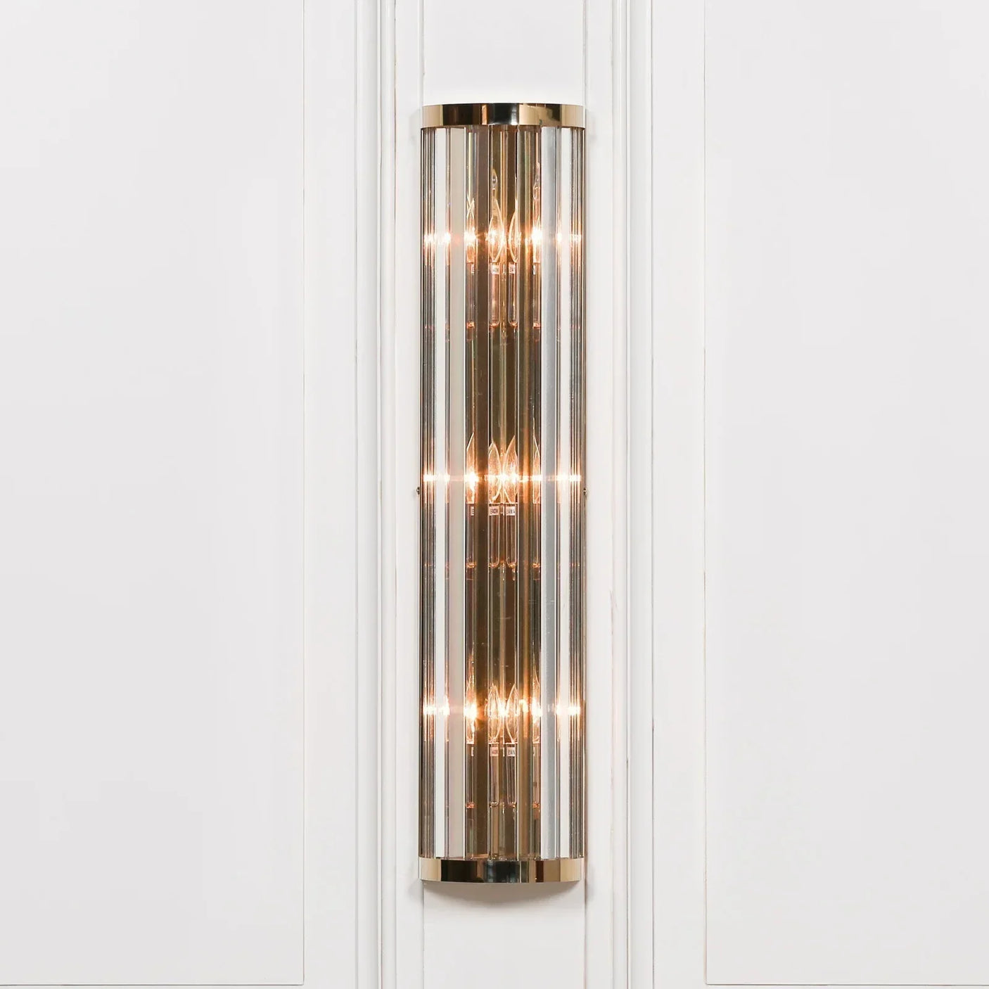 Modern wall light with gold and glass detail mounted on white panelled wall