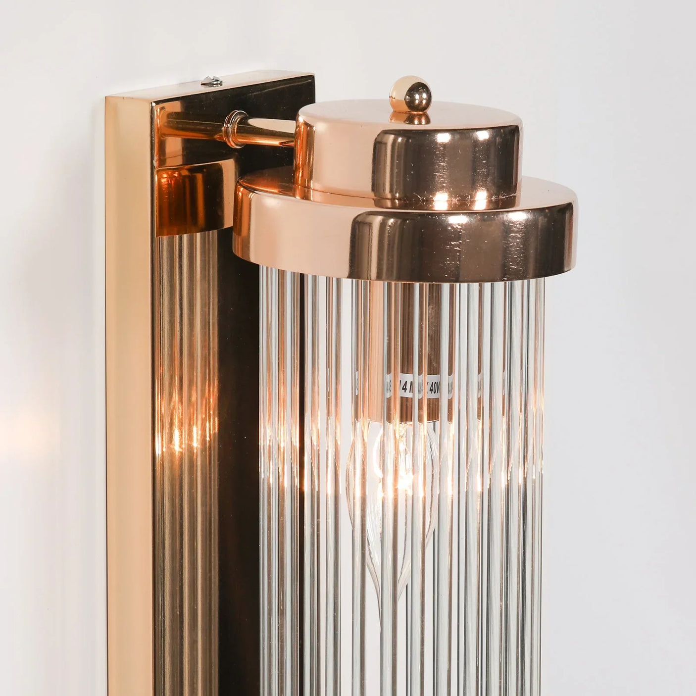 Gold wall light with ribbed glass shade and exposed bulb on white background