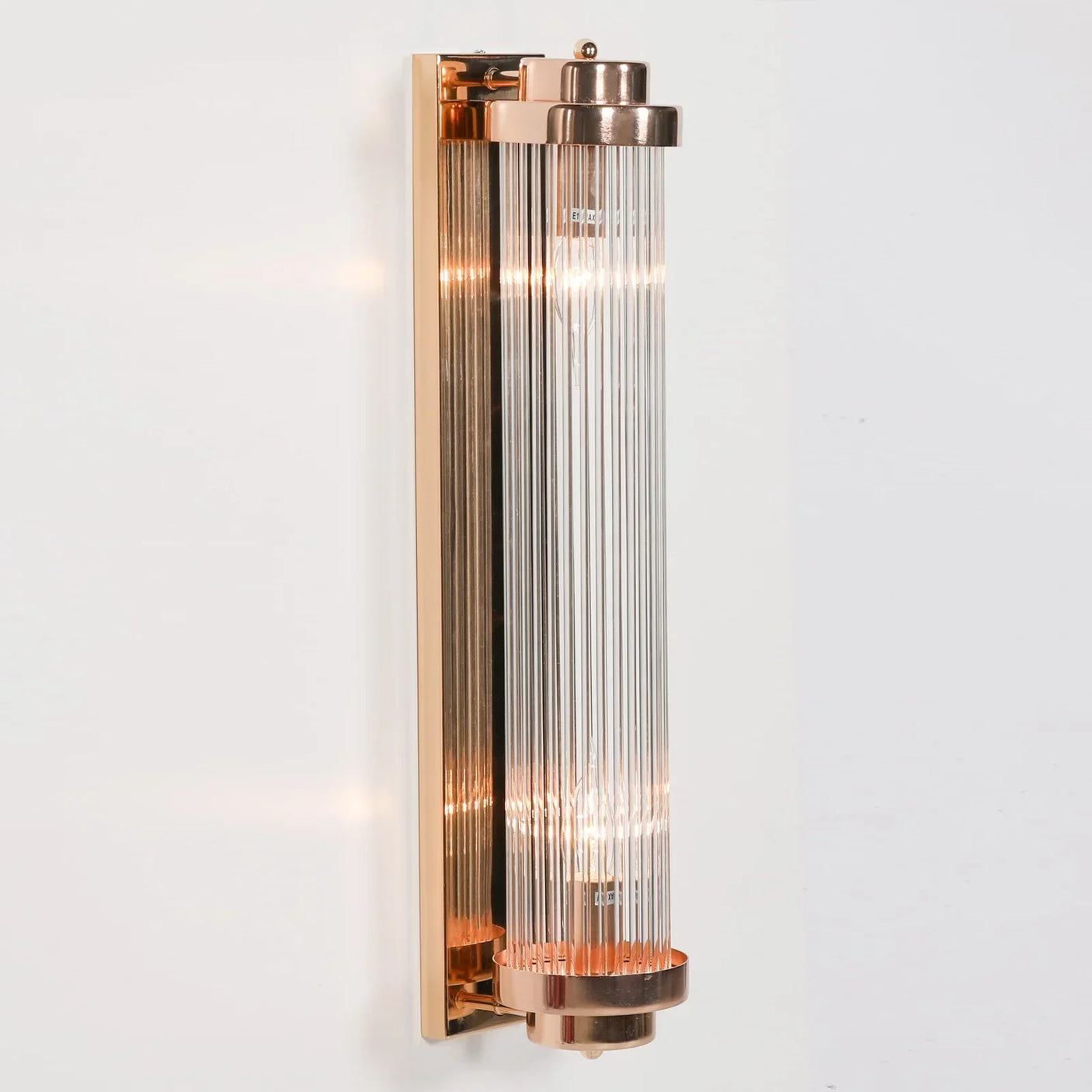 Gold wall light with vertical glass rods mounted on white wall