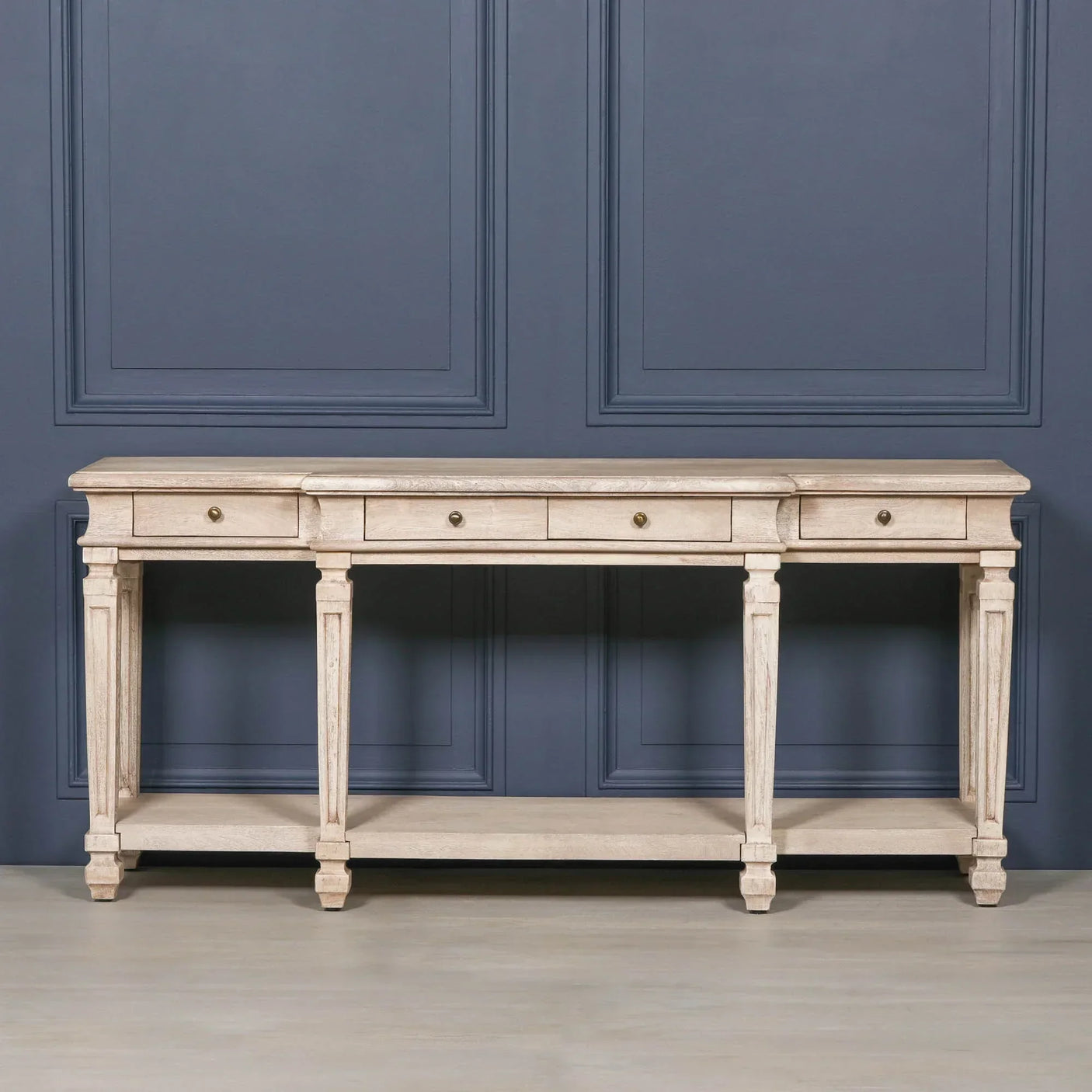Light wood console table with drawers and lower shelf, set against blue panel wall