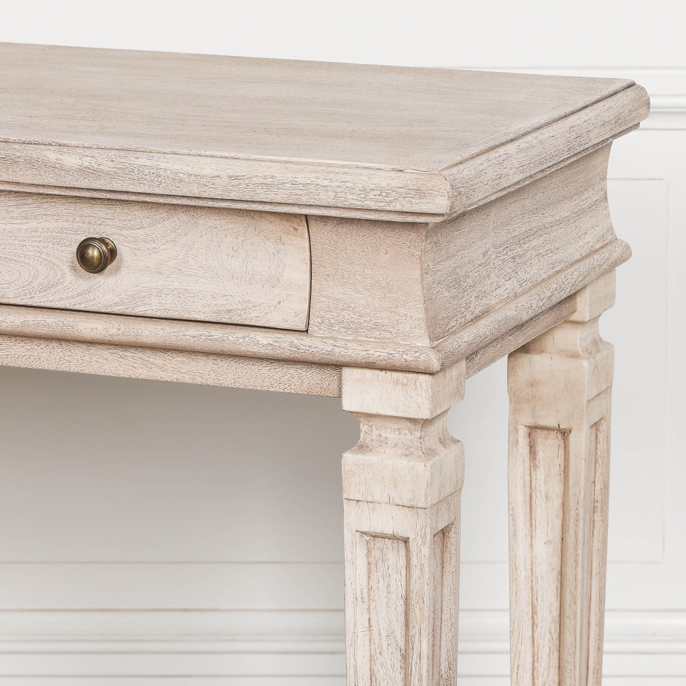 Light wood console table with single drawer and carved legs against white wall