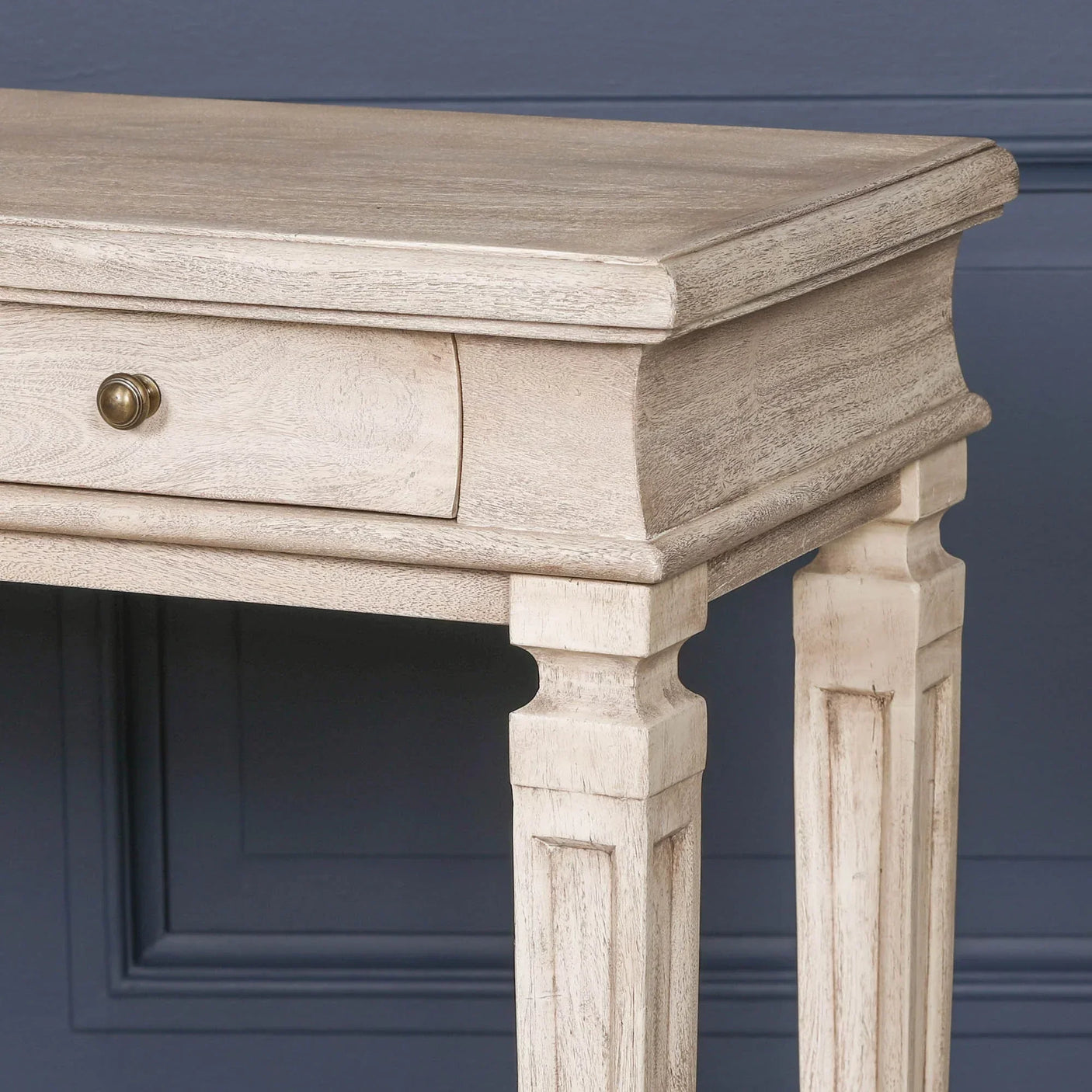 Light wood console table with single drawer and brass knob against dark blue wall