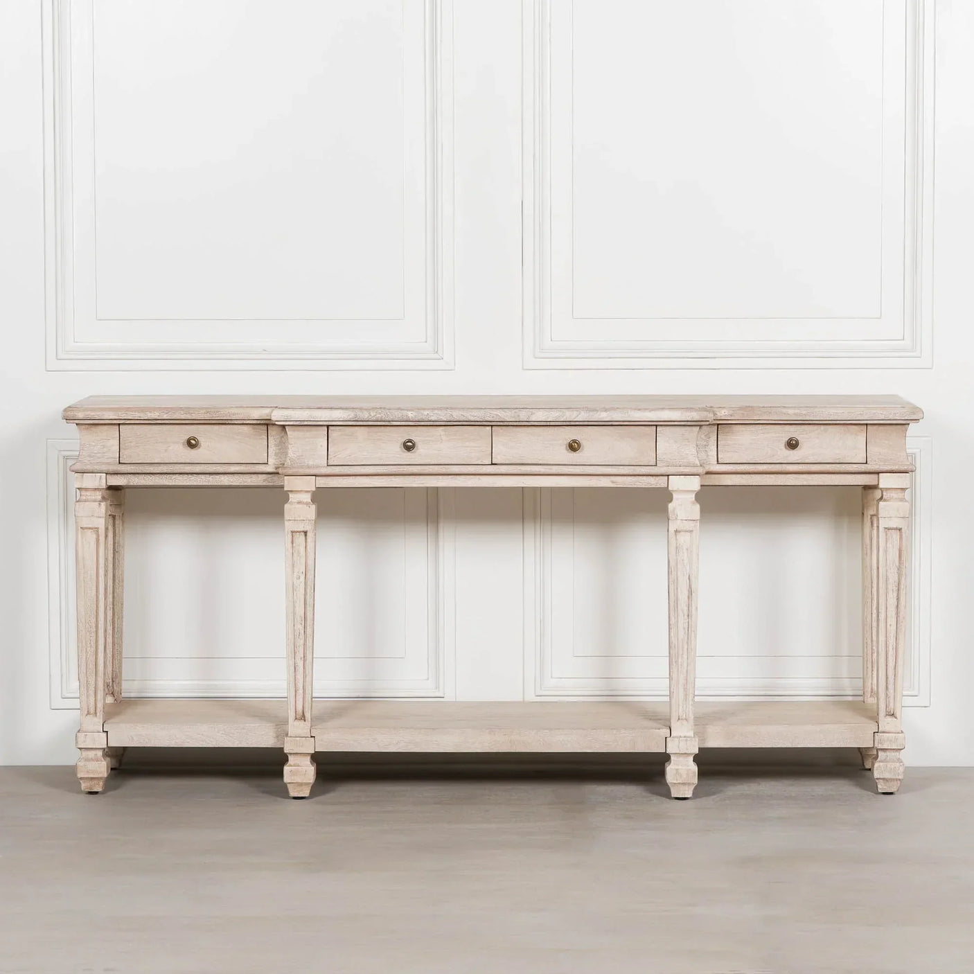 Light wood console table with four drawers and lower shelf against white wall paneling