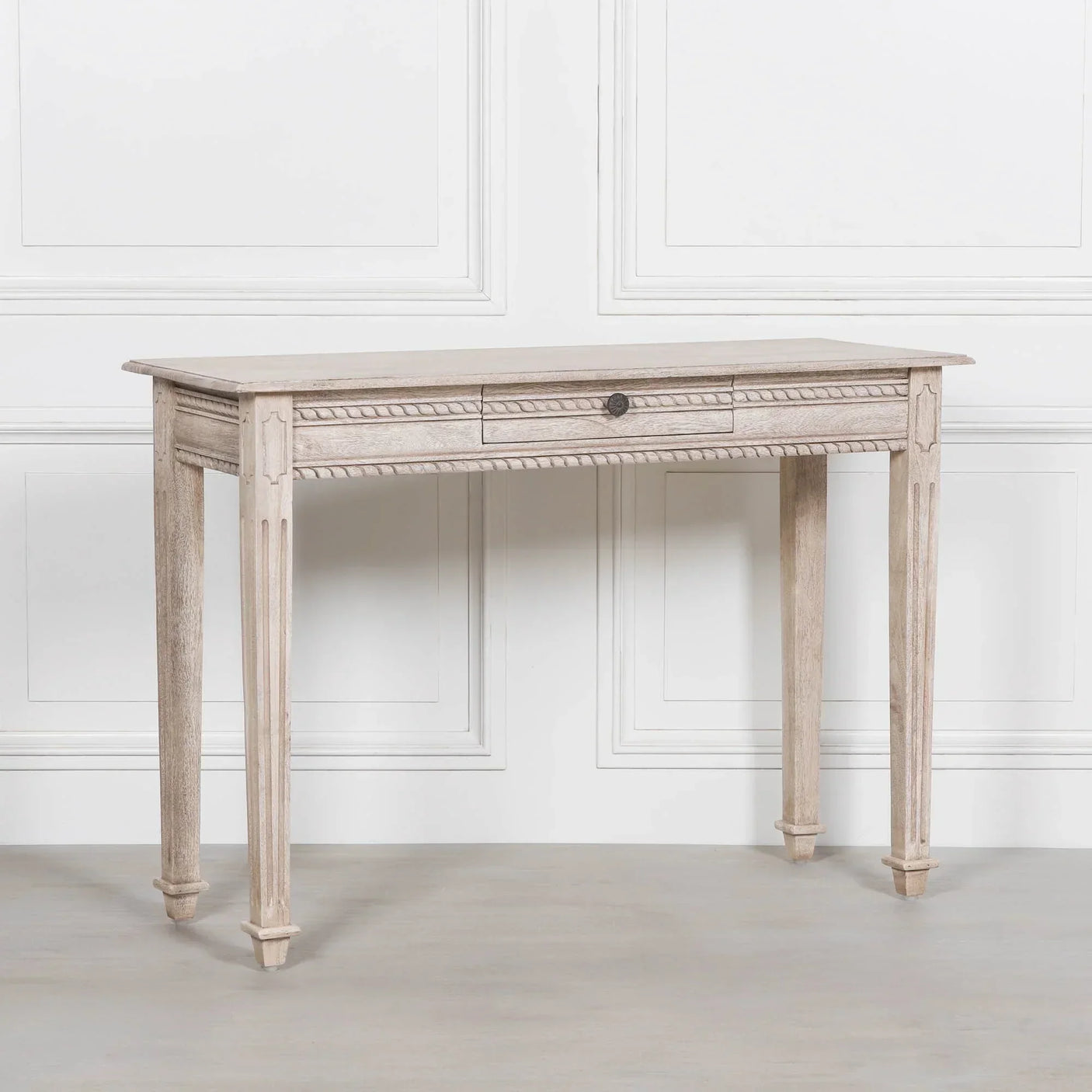 Light wood console table with carved legs and single drawer against white panelled wall