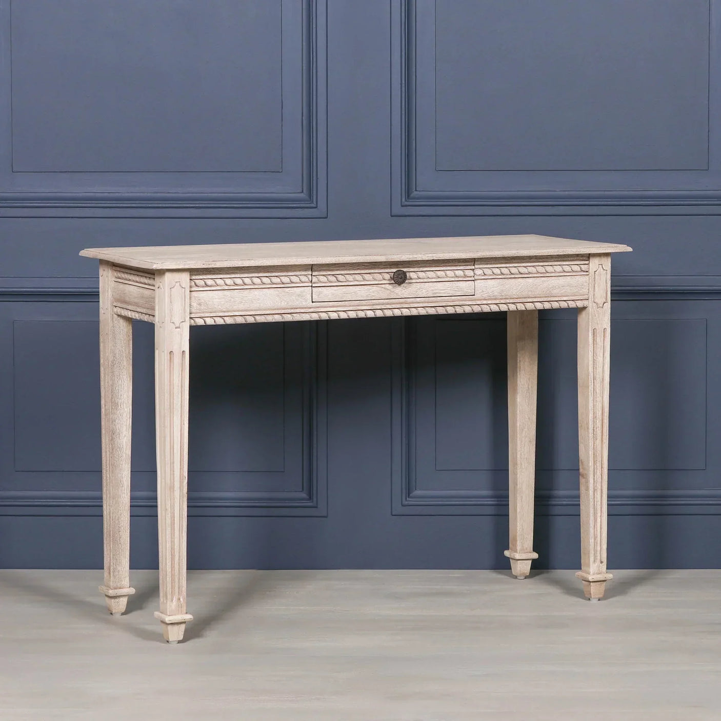 Light wood console table with single central drawer and carved legs against blue panel wall