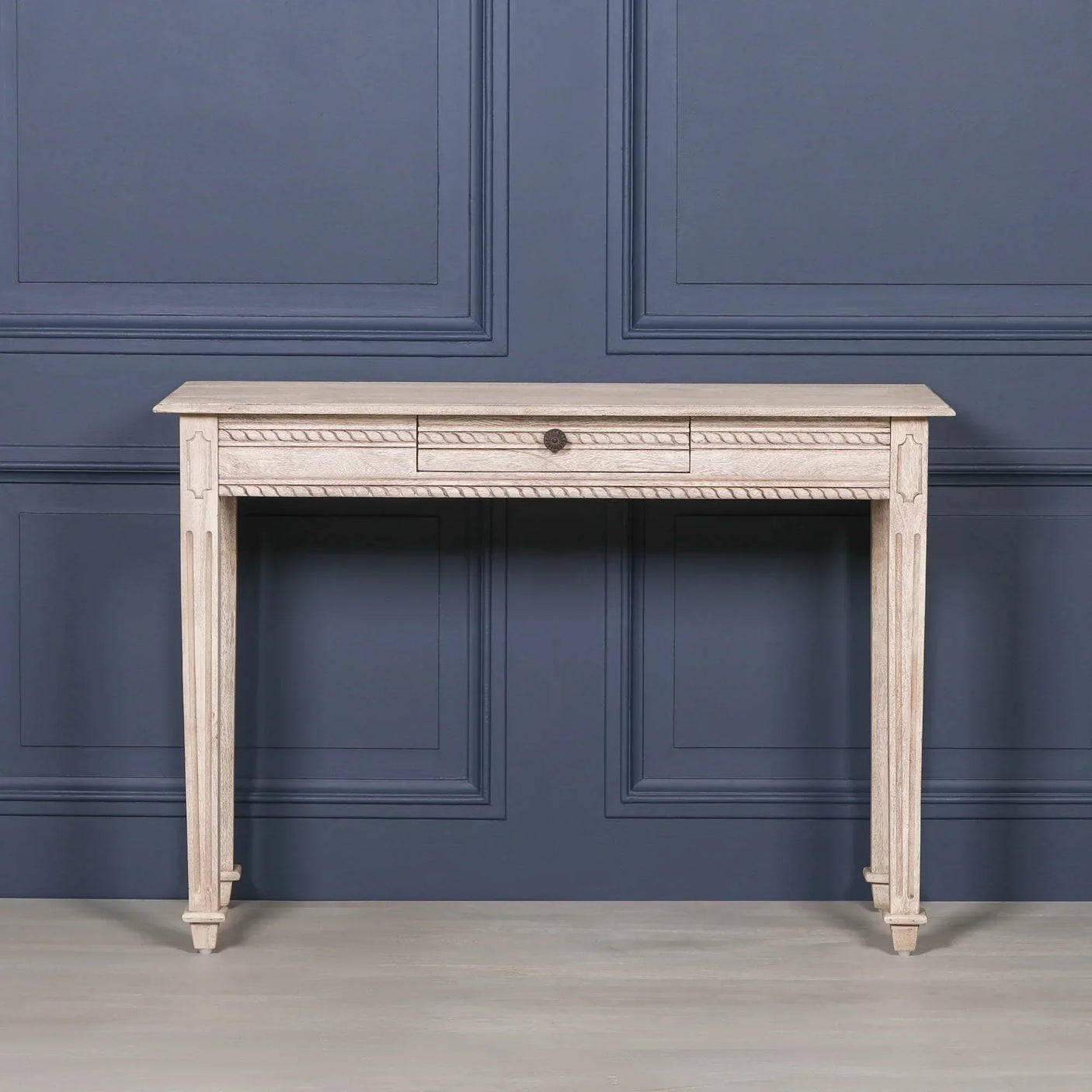 Light wood console table with carved legs and single drawer against blue panel wall