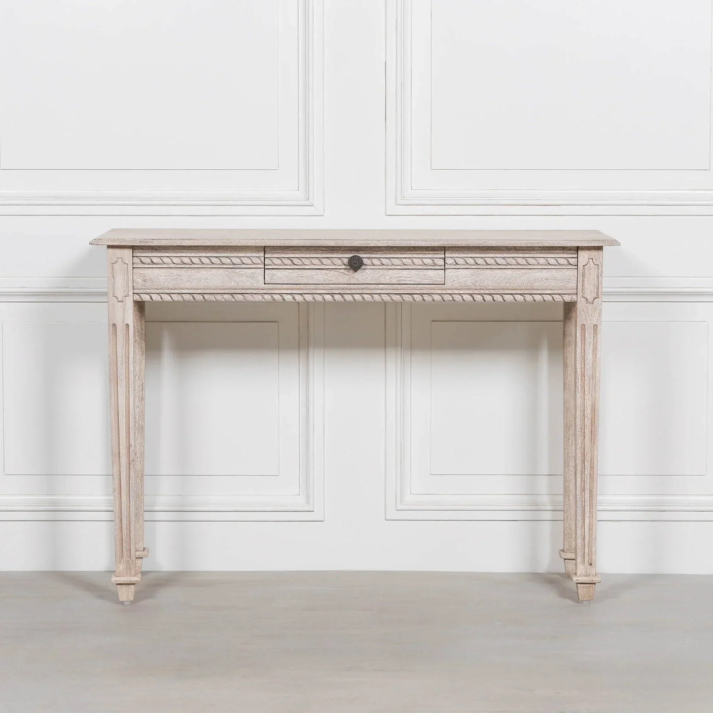 Light wood console table with carved detail and single center drawer against a white wall